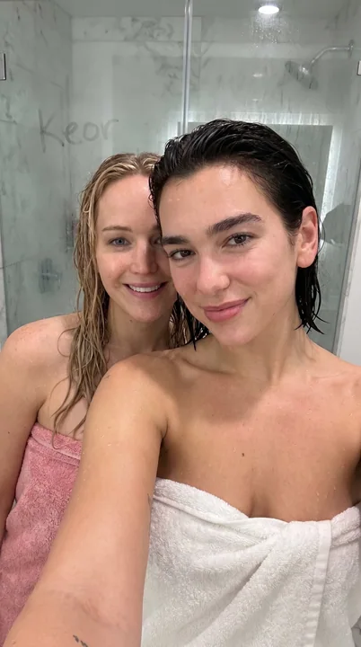 Dua Lipa and Jennifer Lawrence pose together soaking wet in a bathroom photo