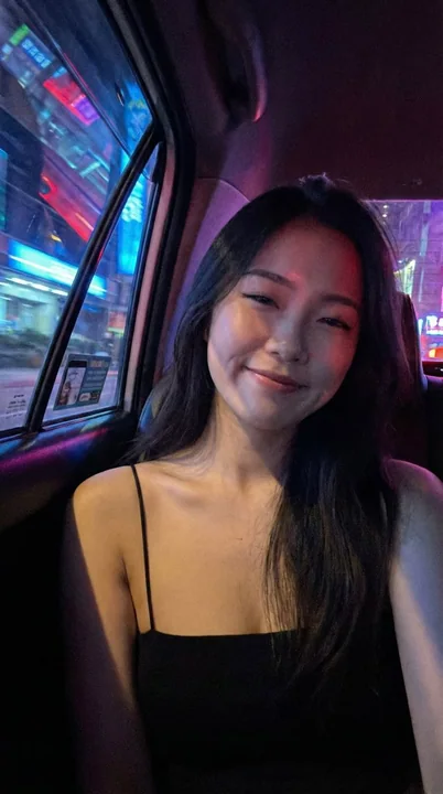 ネオンが輝く夜の下、タクシーの後ろ座席でセルフィーを撮る少女