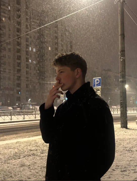 Le profil triste d'une personne fumant sous la lumière de la rue par une nuit d'hiver enneigée