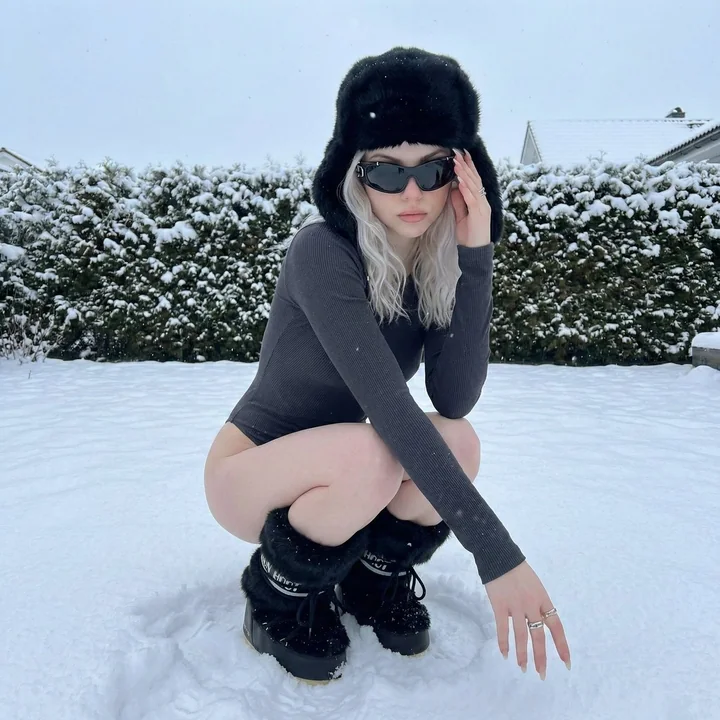氷のようなプラチナブロンドの少女が雪の中でしゃがむ、クールなファッション大作