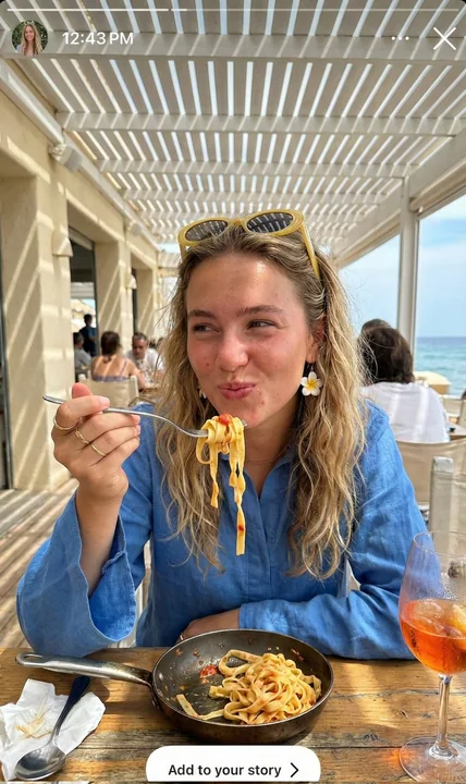 Une jeune vacancière méditerranéenne enroulant des spaghettis sous une lumière du soleil tachetée.